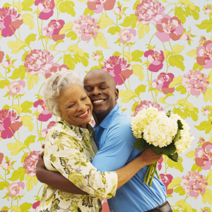 An elderly woman in a floral blouse warmly hugs a smiling man holding a bouquet of white flowers; a heartwarming scene with curated gifts ideal for Mother's Day.