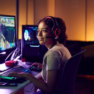 Young woman in a headset gaming at a dual-monitor setup in a cozy, dimly lit room; a perfect gift for gamers.